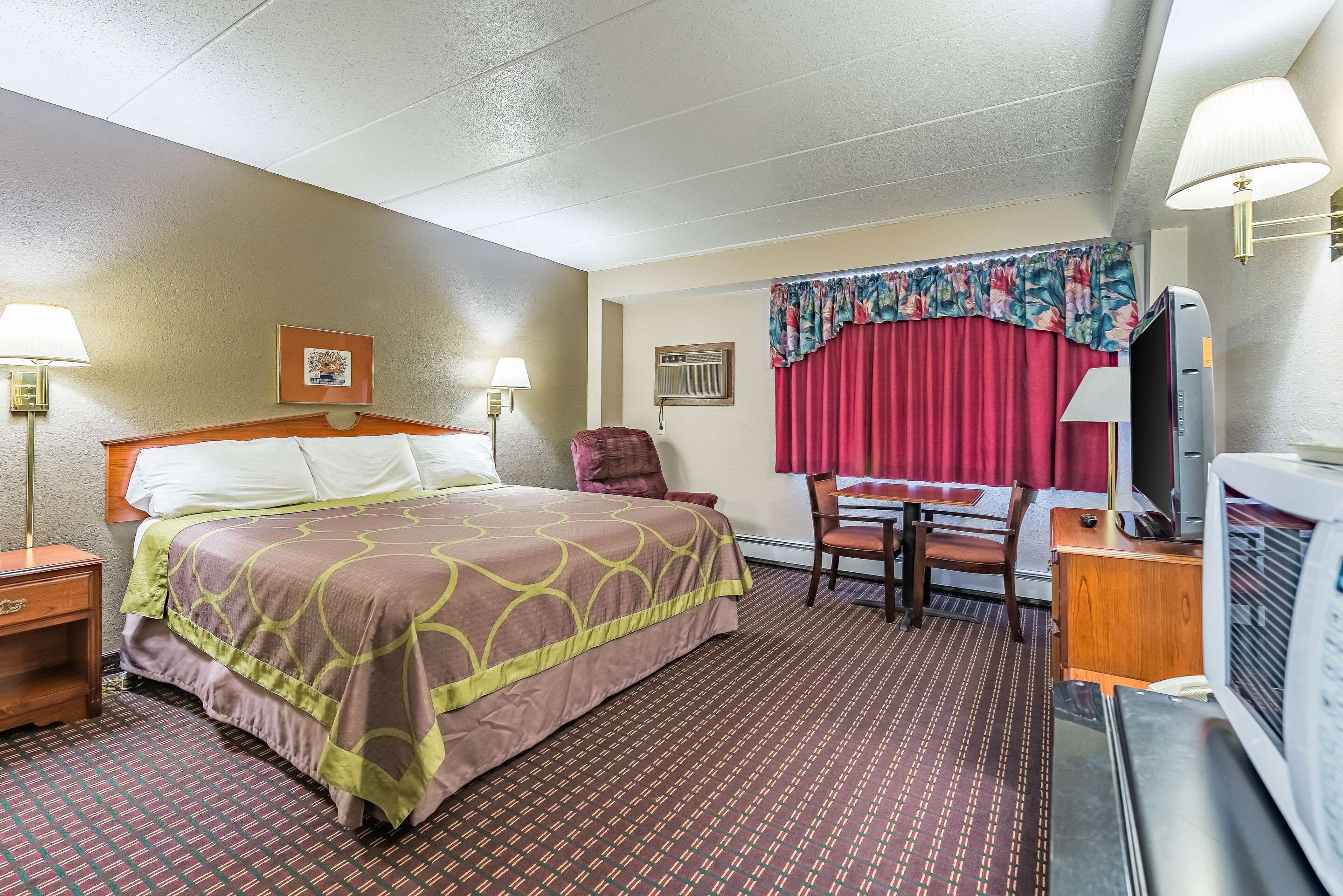 A hotel room with a bed, a desk with a chair, a television, and a microwave.