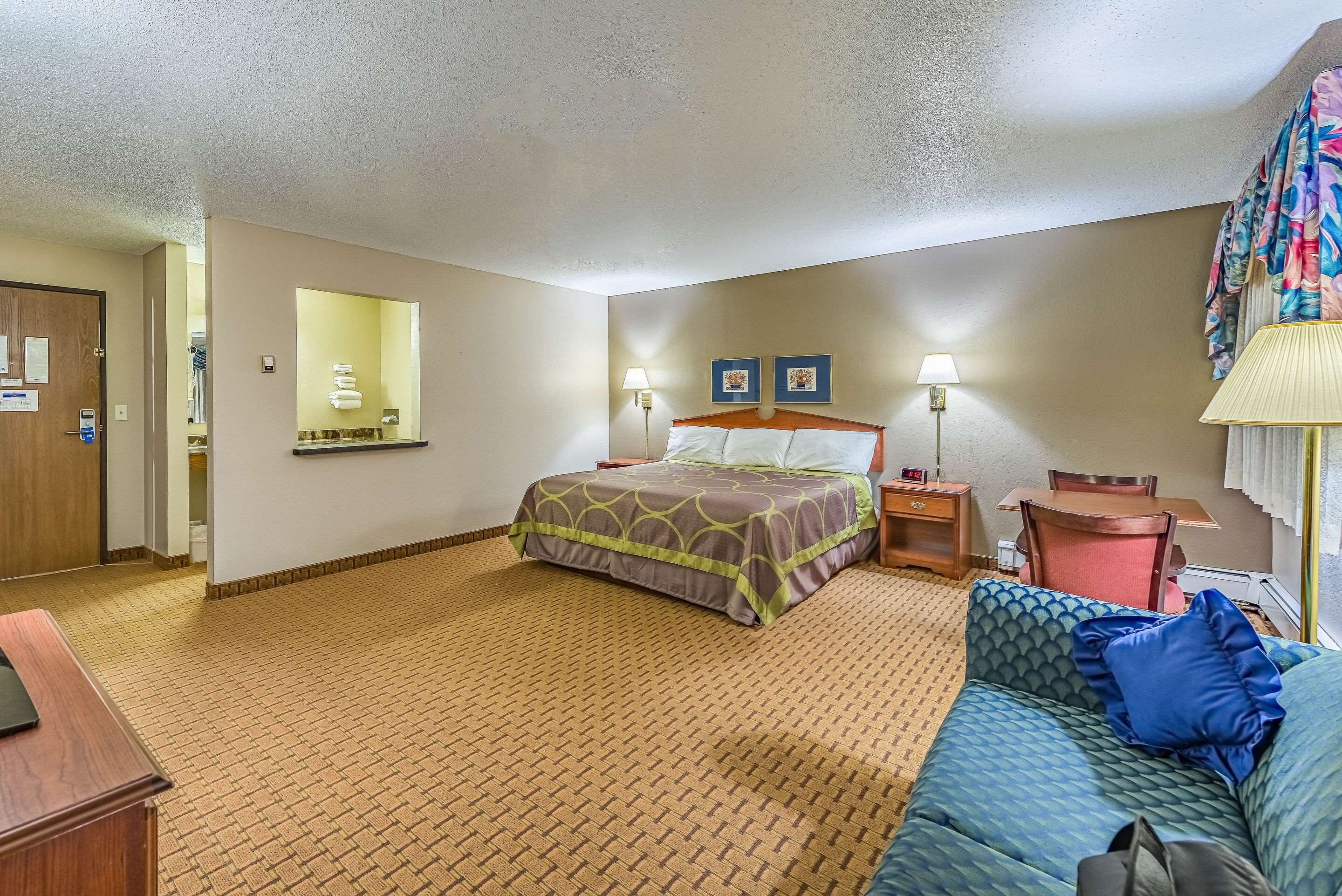 A hotel room with a bed, a sofa, a desk, and a mirror.