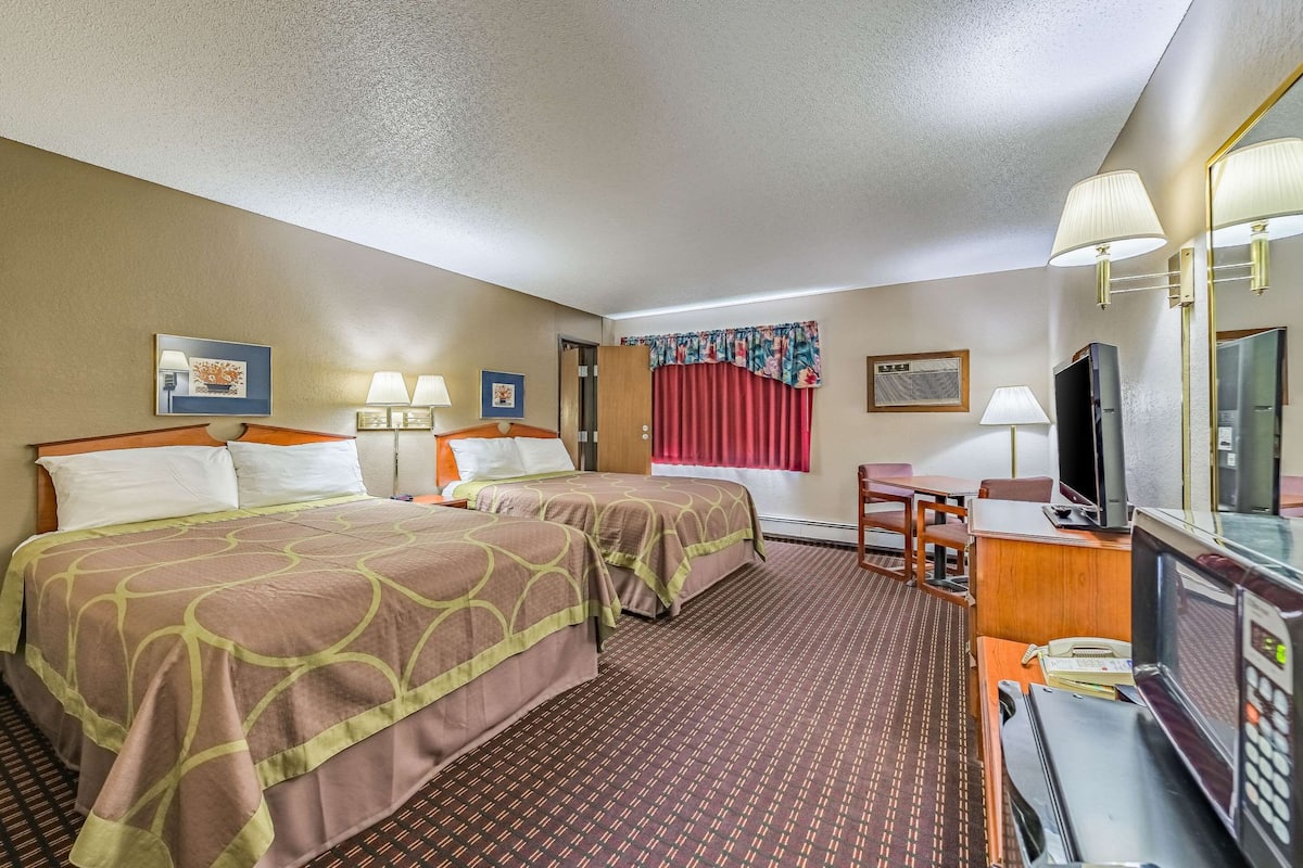 A hotel room with two beds, a desk with a computer, a TV, and a mirror.