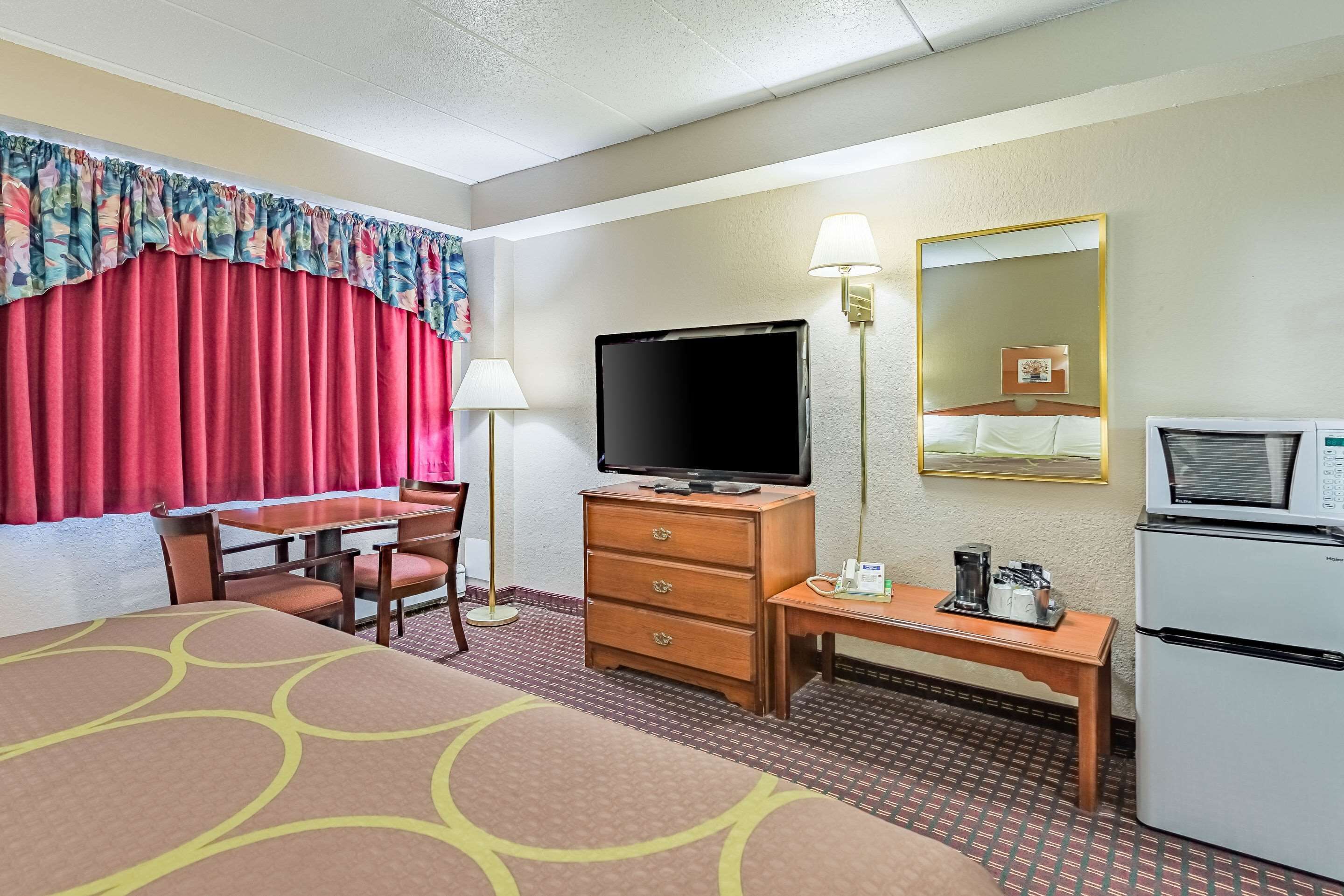 Una habitación de hotel con una cama, un escritorio con televisor, un refrigerador y un espejo.