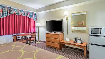 Una habitación de hotel con una cama, un escritorio con televisor, un refrigerador y un espejo.