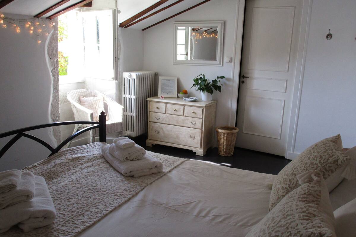 Une chambre à coucher comprenant un lit, une commode, un radiateur, un miroir et un panier en osier.