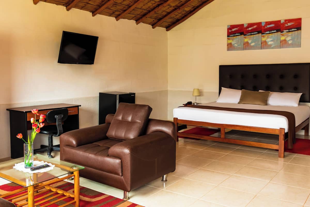 Ein Hotelzimmer mit braunem Ledersofa, einem Bett mit weißen Leinen, einem an der Wand montierten Flachbildfernseher und einem kleinen Schreibtisch mit Telefon.