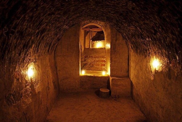 A dimly lit, circular stone room with a central window and a wooden stool. - QALA Hotel & Resorts (Grocio Prado)