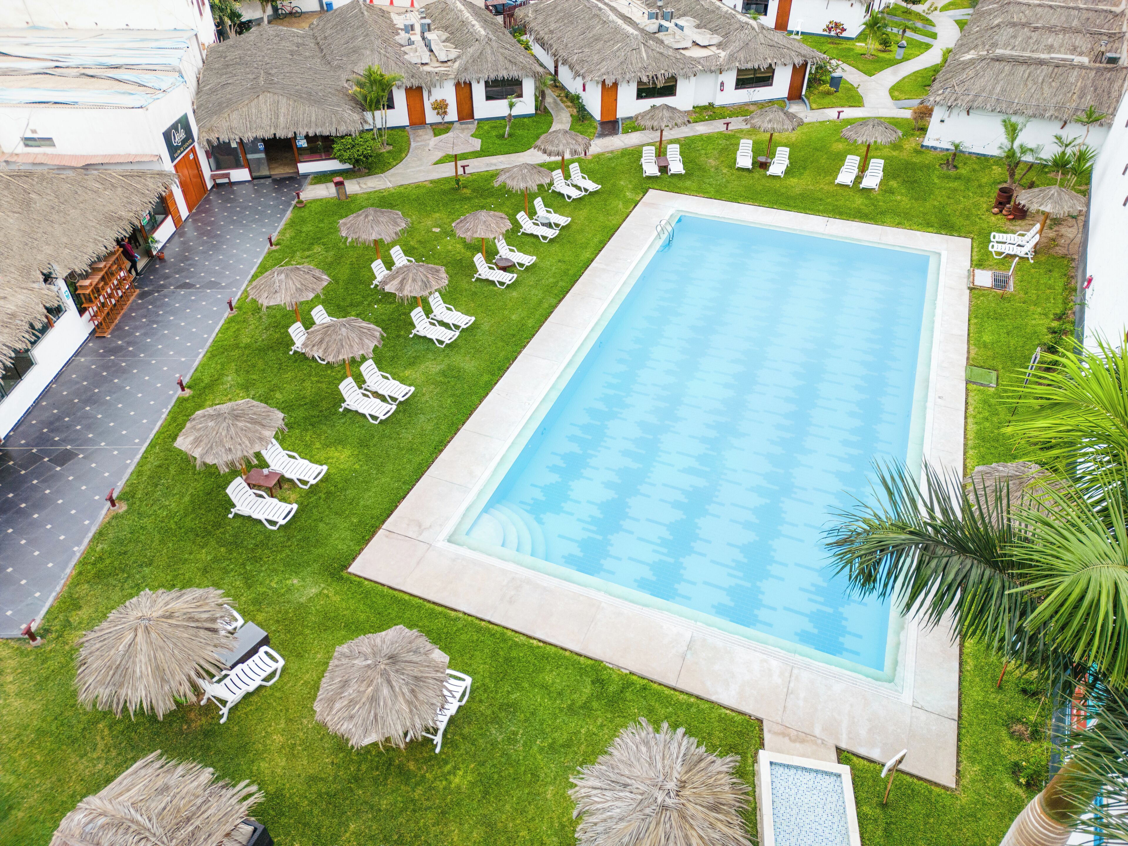 A swimming pool surrounded by white lounge chairs and thatched umbrellas, with a building in the background.