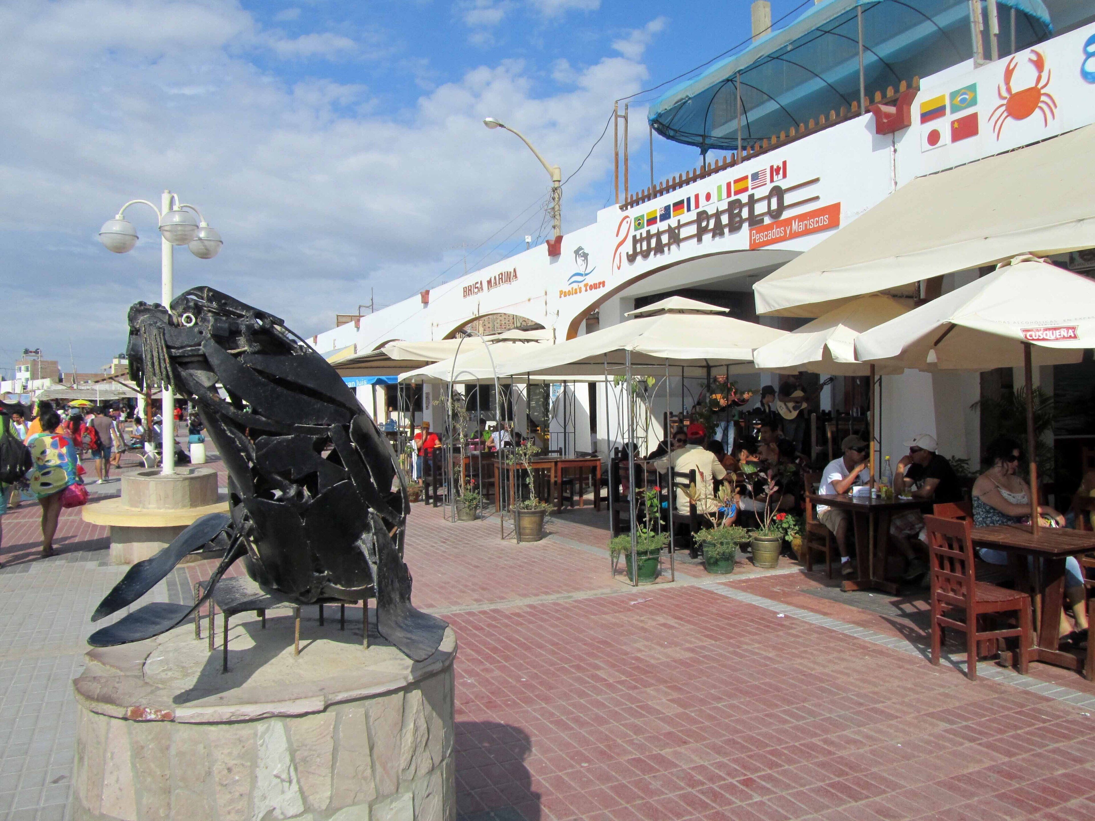 A public square with a sculpture, outdoor seating, and a seafood restaurant.