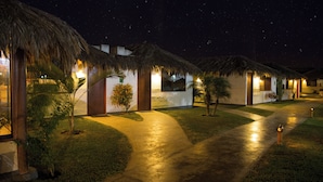 A row of thatched-roof cottages with a paved walkway and small trees, under a starry night sky. - QALA Hotel & Resorts (Grocio Prado)