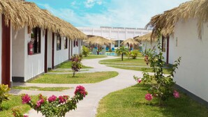 A pathway leading to thatched-roof buildings with a pool area in the background. - QALA Hotel & Resorts (Grocio Prado)