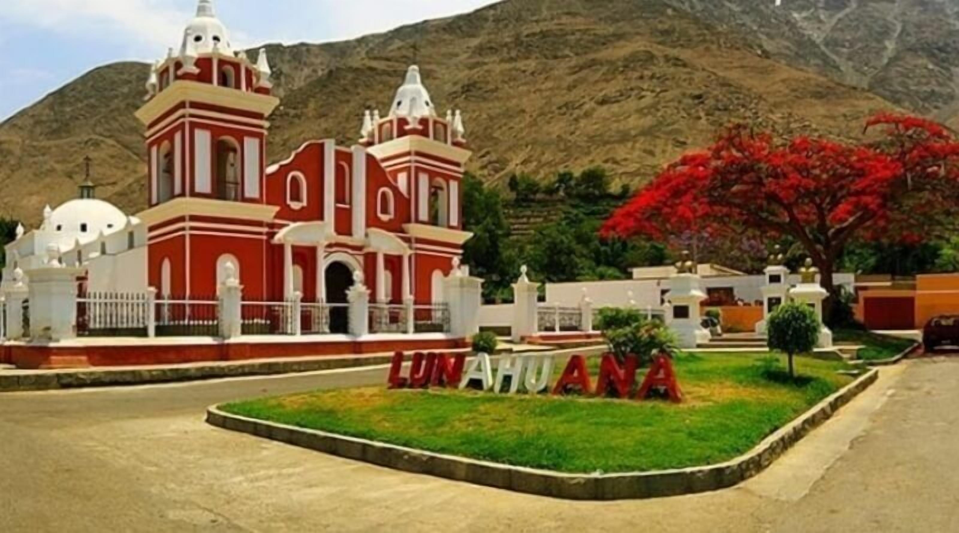 A church with a red facade and white accents, surrounded by a well-maintained lawn and a large red tree.