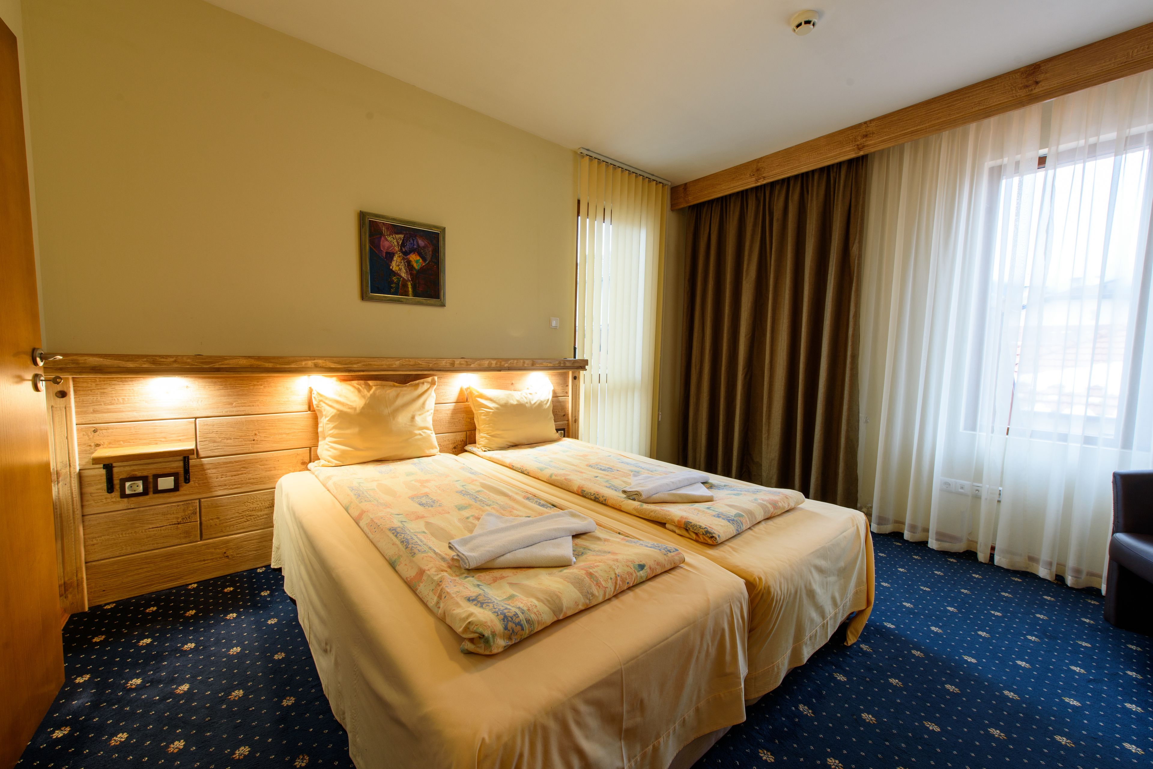 Habitació d'hotel amb dos llits, un capçal de fusta, un quadre a la paret i una finestra gran amb cortines.