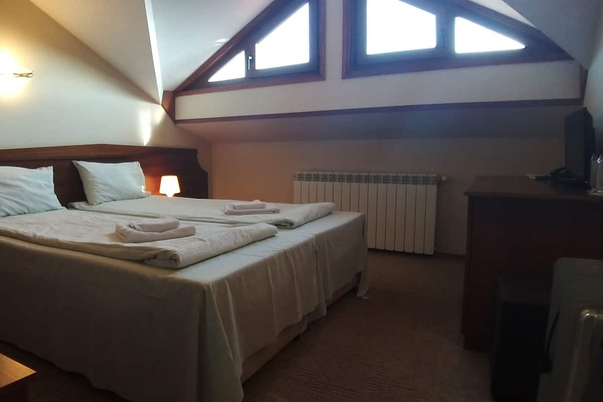 A bedroom with two beds, a radiator, a desk, and a TV.