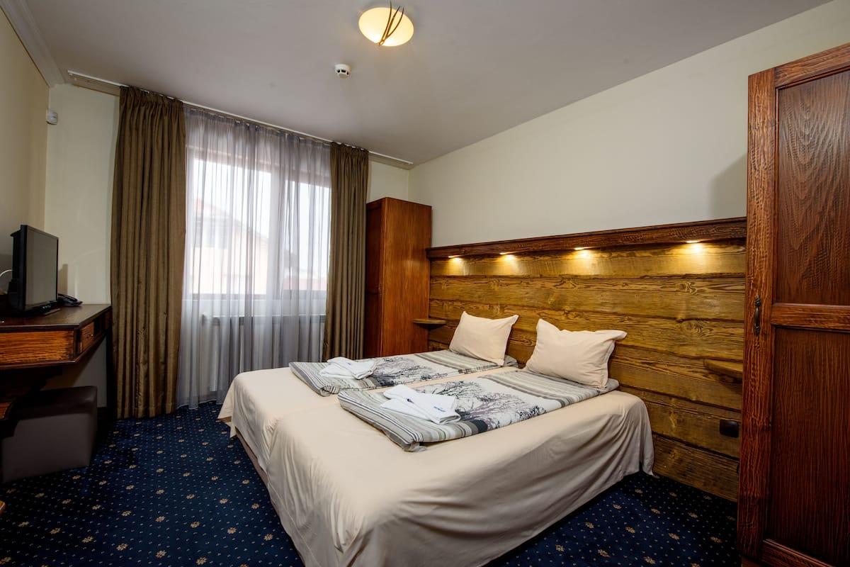 A hotel room with a large bed, a wooden headboard, a desk with a television, and a window with curtains.
