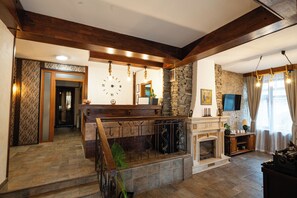 A spacious living area with a fireplace, stone wall, and wooden beams. - Kap House Hotel (Bansko)