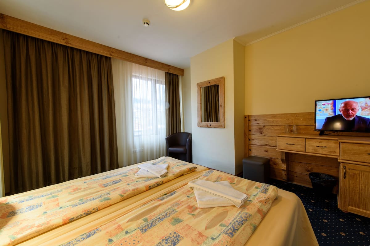 A hotel room with two beds, a wooden desk, a television, and a window with curtains.