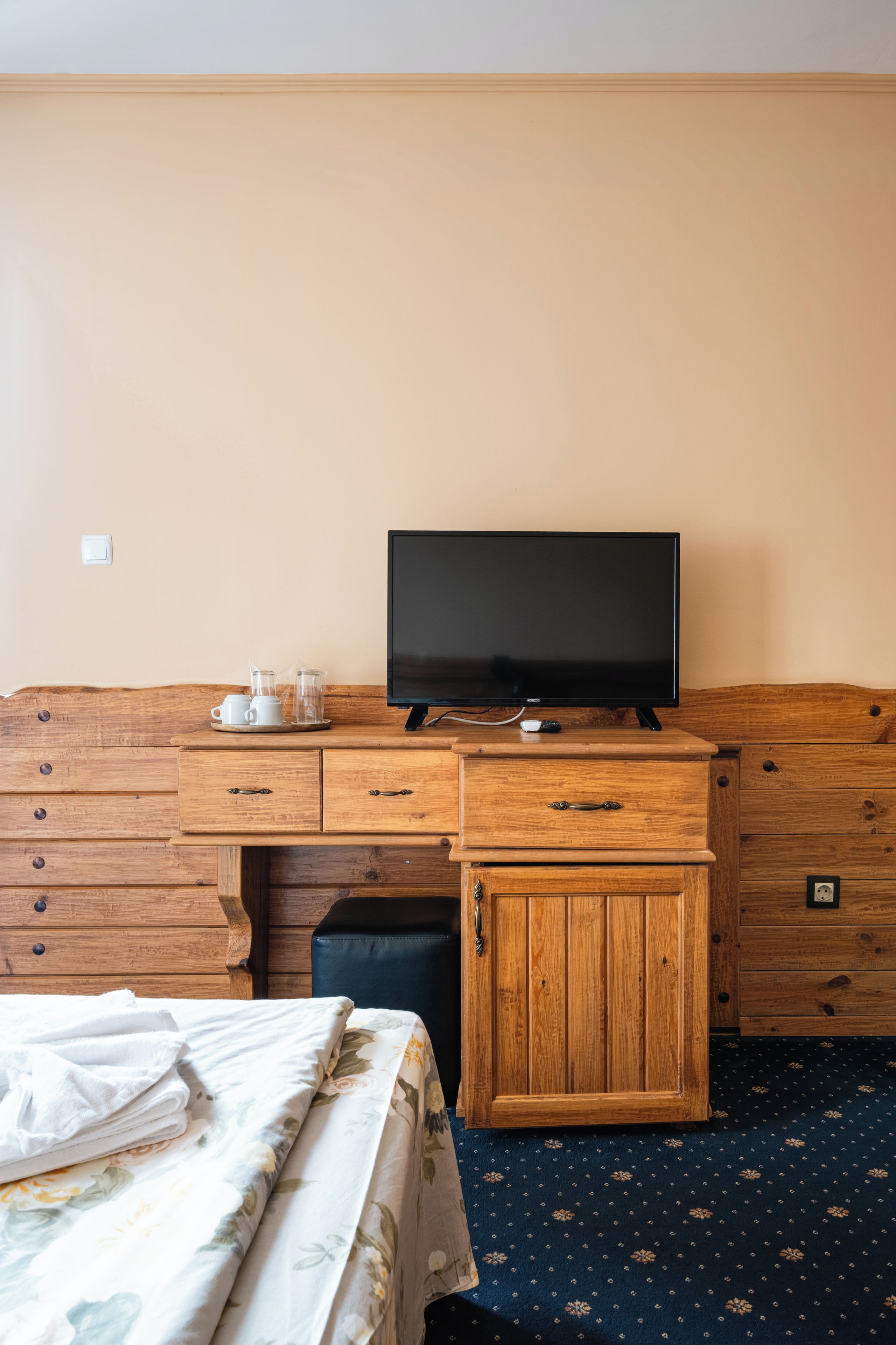 Ein Hotelzimmer mit einem Holzkapuzen-Schrank, einem Fernseher und einem Bett mit einer blumigen Tagesdecke.