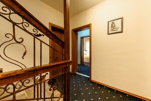 A staircase with ornate metal railings leading to a room with a patterned carpet and a framed picture on the wall.