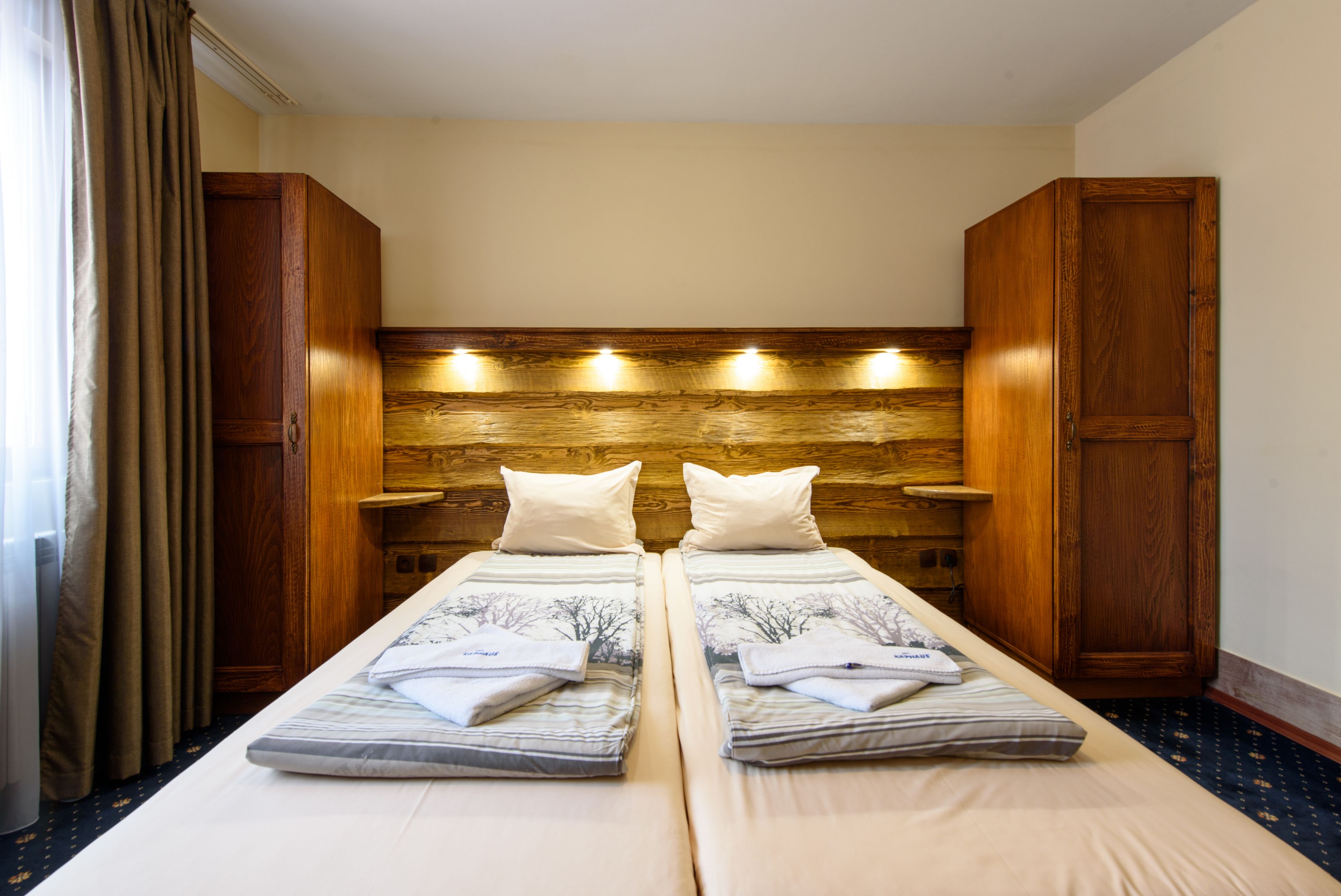 A twin room with two beds, wooden headboard, bedside tables, and a window with curtains.