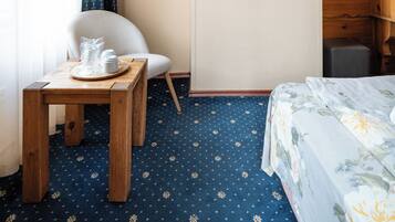 A hotel room with a wooden bed, a small table with cups, a chair, a mirror on the wall, and a patterned carpet.