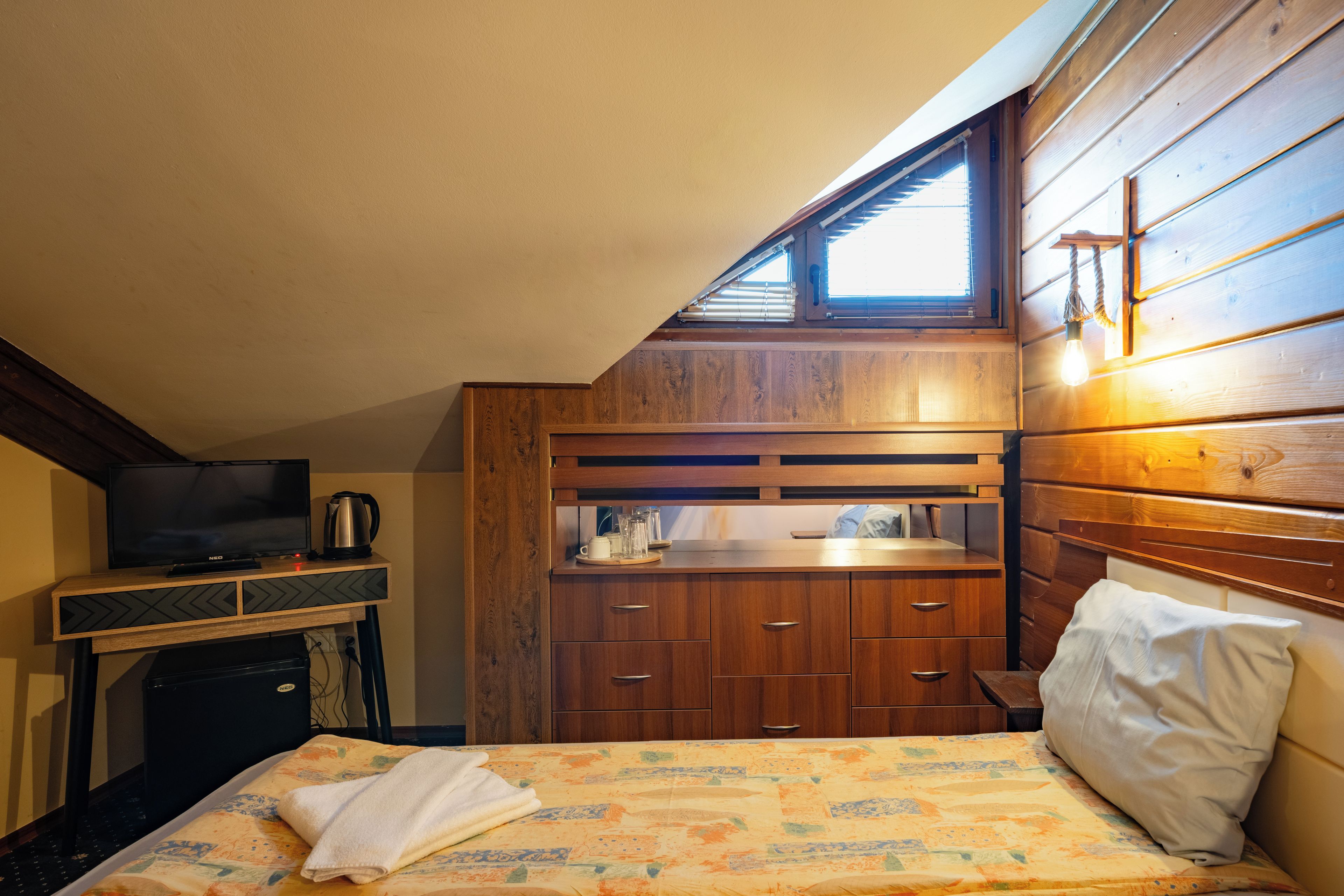A bedroom with a bed, a television, a kettle, and a window.