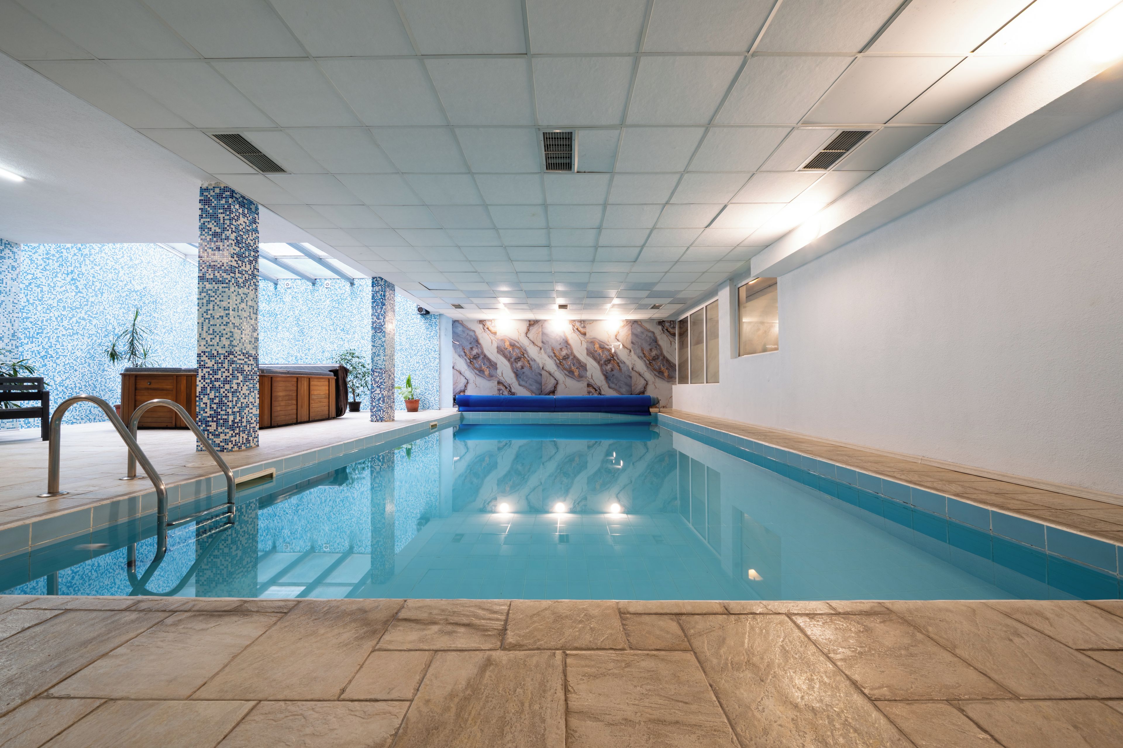 An indoor swimming pool with clear water, tiled walls, and a wooden deck area.