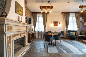 A living room with a fireplace, a dining area with chairs, a table, and a view of the outdoors through large windows. - Kap House Hotel (Bansko)