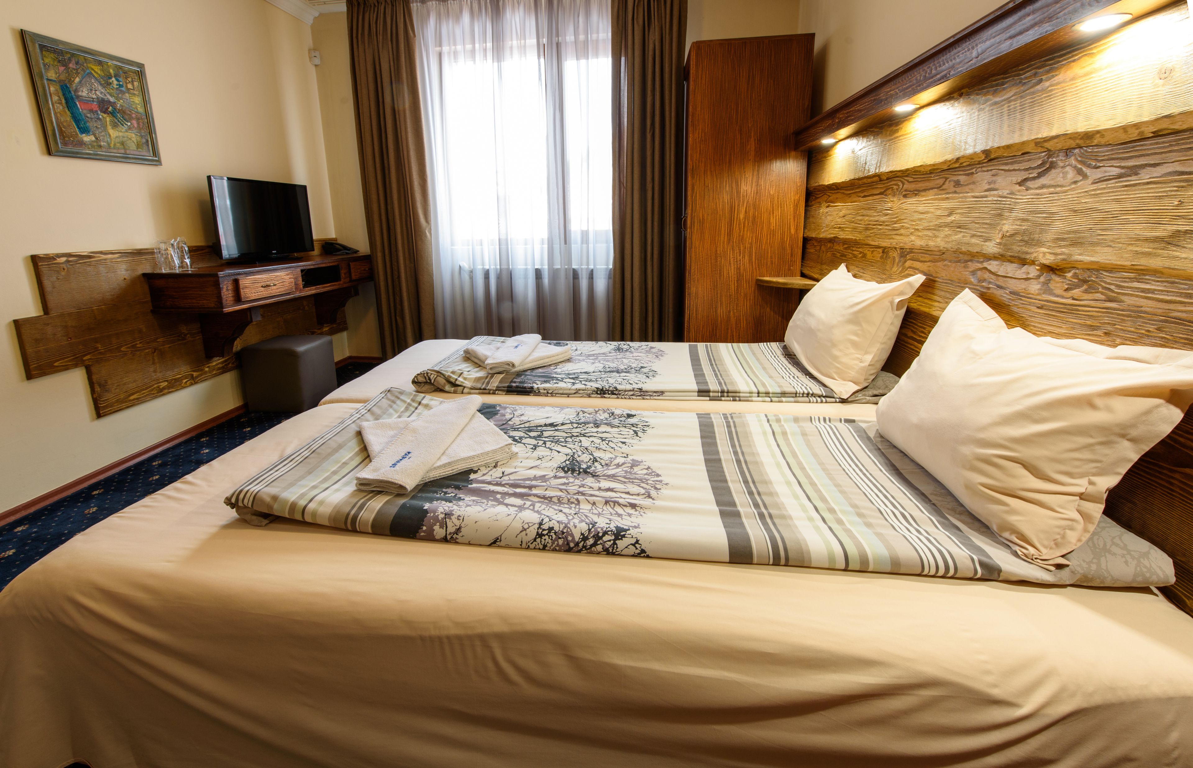 Habitación de hotel con dos camas, un televisor sobre un escritorio de madera y un ventanal con cortinas.