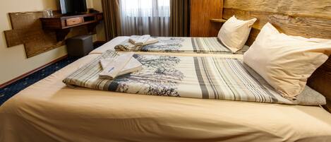 Habitación de hotel con dos camas, un televisor sobre un escritorio de madera y un ventanal con cortinas.