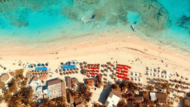 An aerial view of a beach resort with clear turquoise waters, several boats, and a beachfront area with umbrellas and lounge chairs. - Serenity Authentic Glamping Tulum (Xpu-Ha)