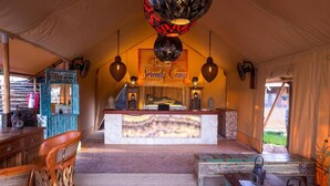 A cozy interior of a tent with a central reception desk, wooden furniture, and hanging lanterns. - Serenity Authentic Glamping Tulum (Xpu-Ha)