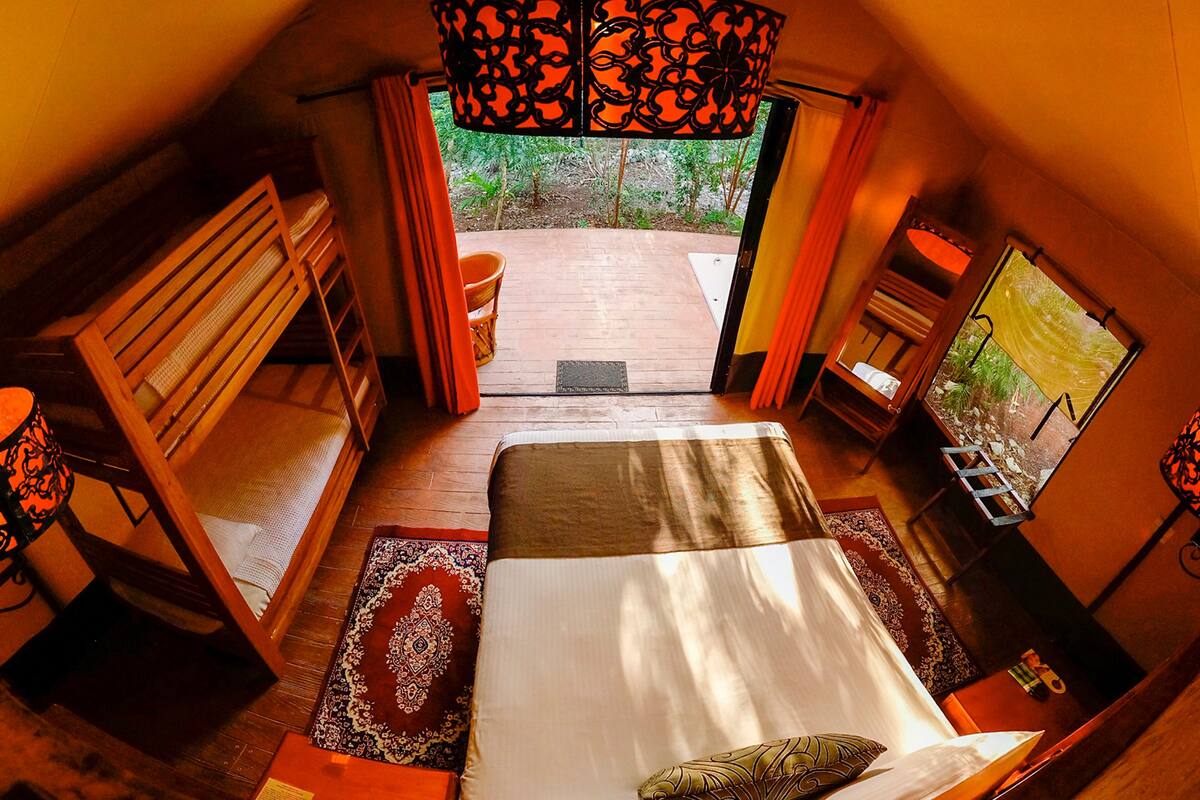 Una habitación acogedora con cama, escritorio y silla. Hay una ventana con cortinas y vistas al verdor exterior.