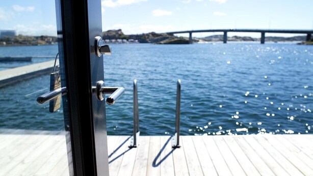 Un muelle de madera con barandillas metálicas y vista a un puente sobre el agua.
