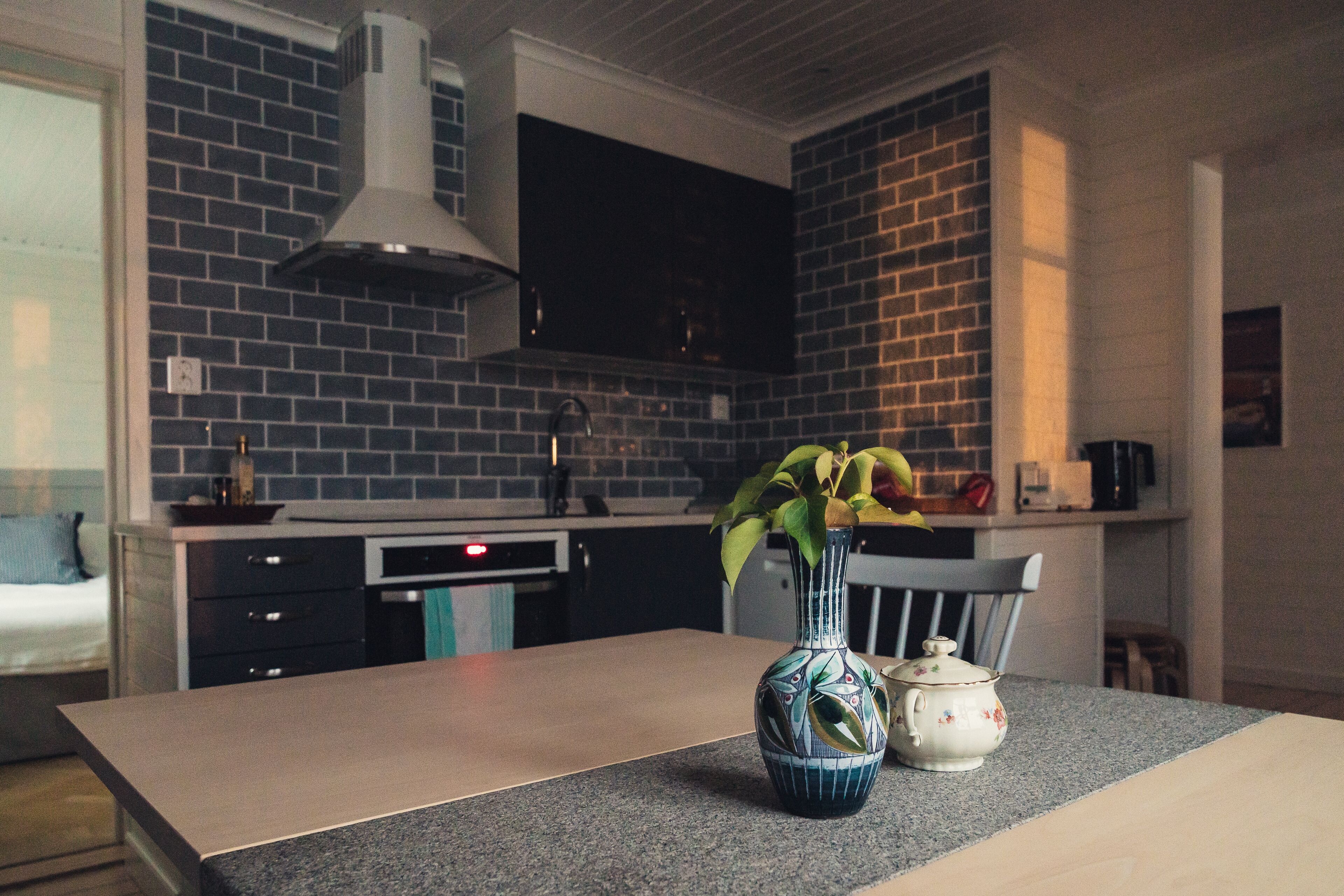 A kitchen with a brick backsplash, a modern stove, and a vase with flowers on the counter.