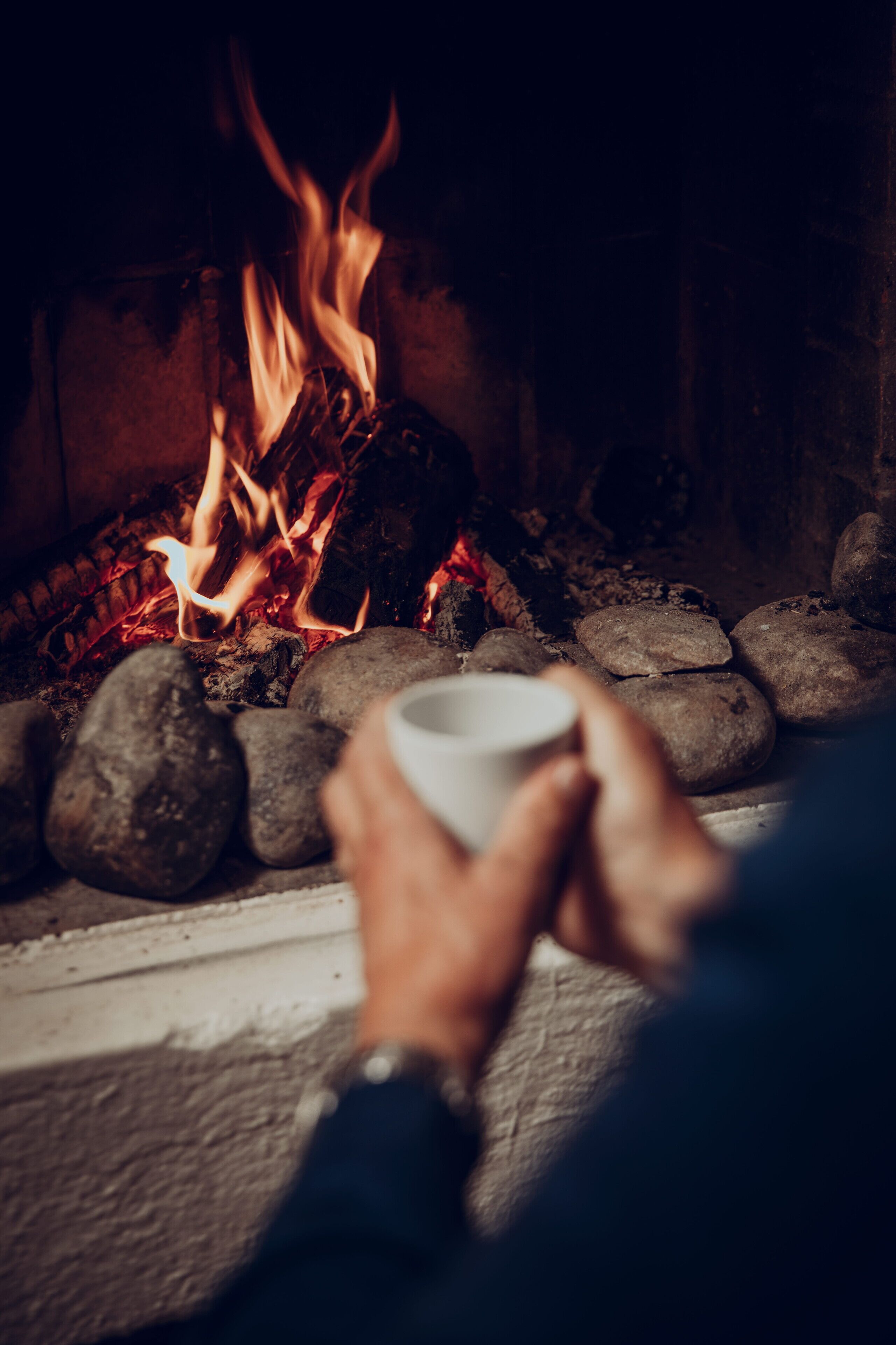 Una chimenea con leña ardiendo y una taza de café.