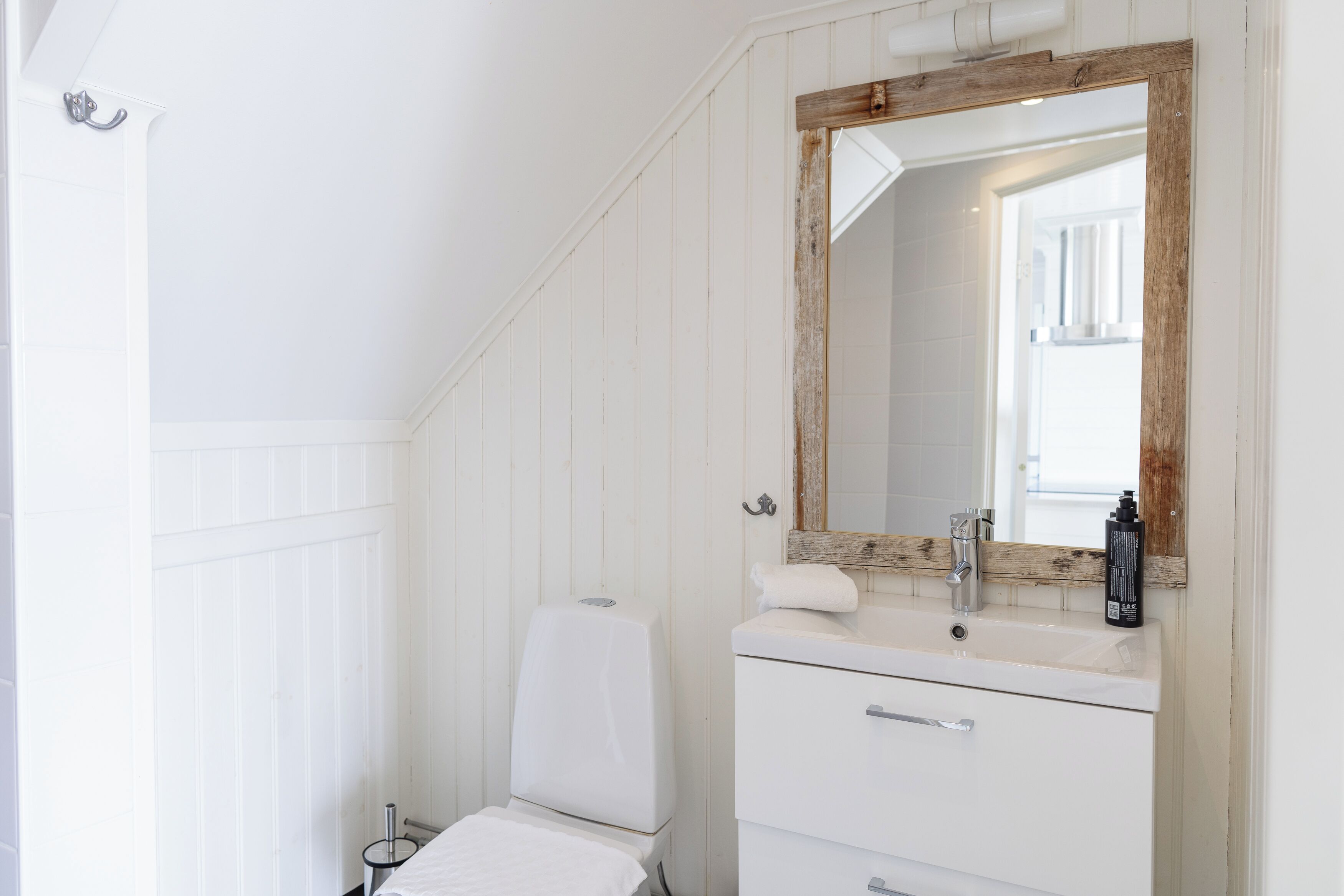 A bathroom with a white vanity, a wooden-framed mirror, and a white toilet.