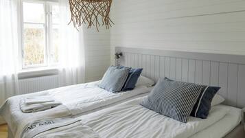 Ein Zimmer mit zwei Betten, weißer Bettwäsche, gestreifteren Kissen, einer Hängeleuchte und einem Fenster mit Jalousien.