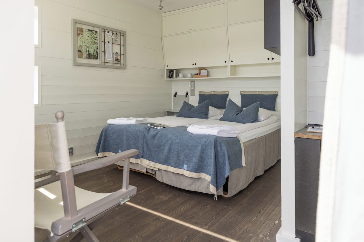 Un dormitorio con cama, una silla, una estantería con objetos y un cuadro en la pared.