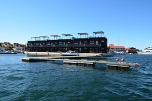 A waterfront building with multiple balconies, docked boats, and a clear blue sky. - Salt & Sill (Klaedesholmen)