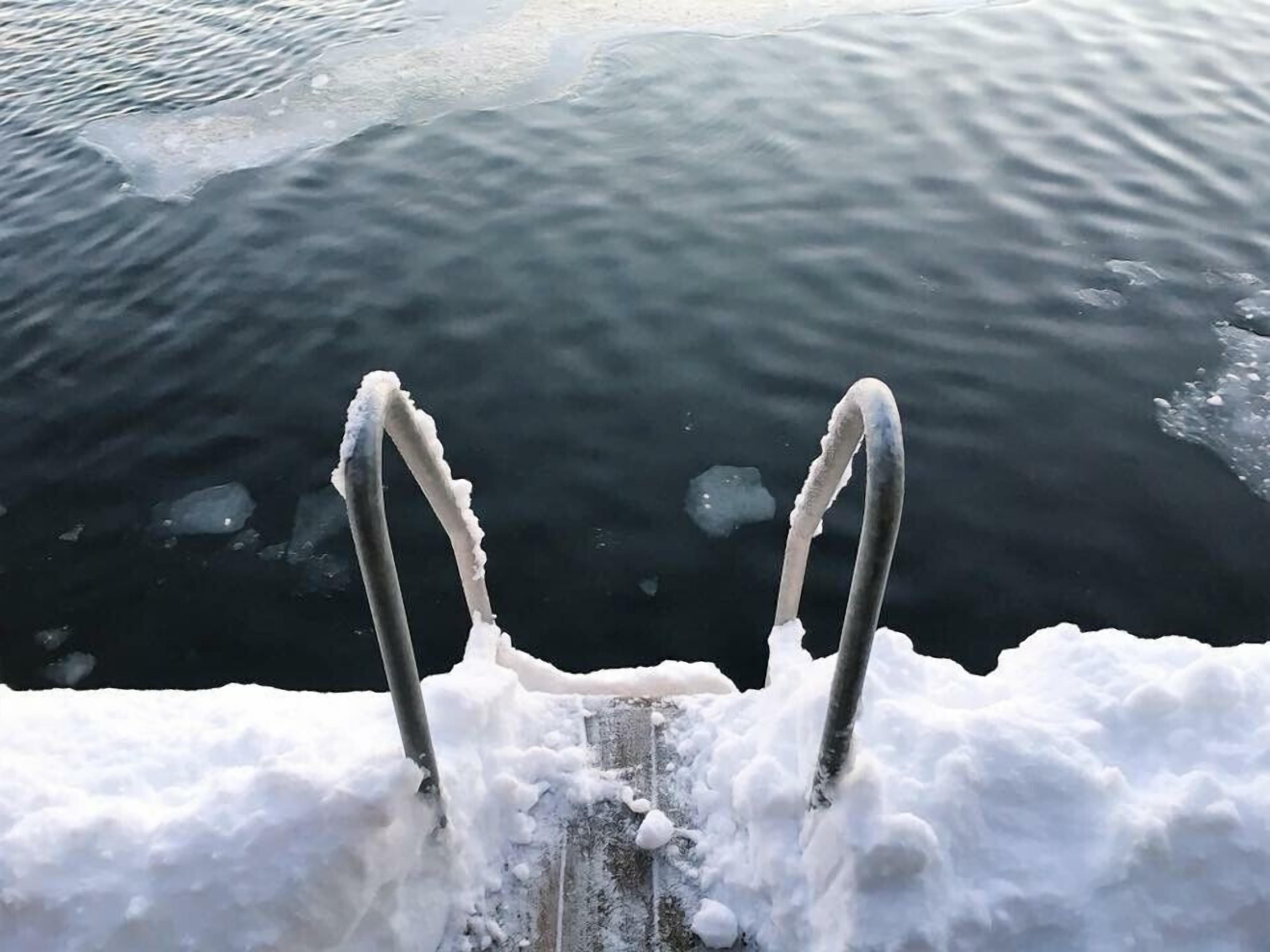 Une échelle métallique menant à une étendue d’eau entourée de glace et de neige.