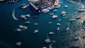 Vista aérea de un pueblo costero con un puerto deportivo lleno de barcos, rodeado de edificios residenciales y pequeñas islas.