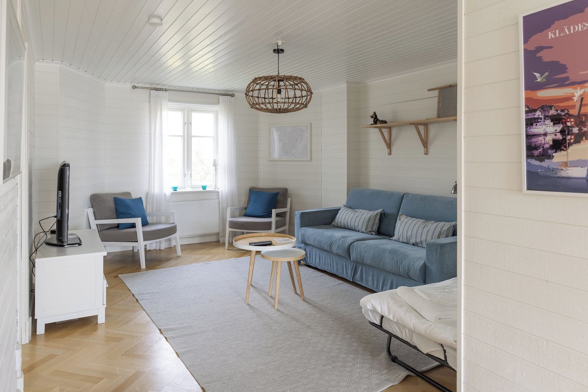 Una sala de estar moderna con un sofá azul, un sofá gris, una mesita auxiliar blanca, una pequeña mesa de madera y una lámpara colgante.