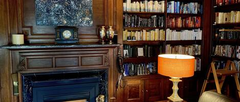 A cozy library with a fireplace, bookshelves, and a decorative lamp.