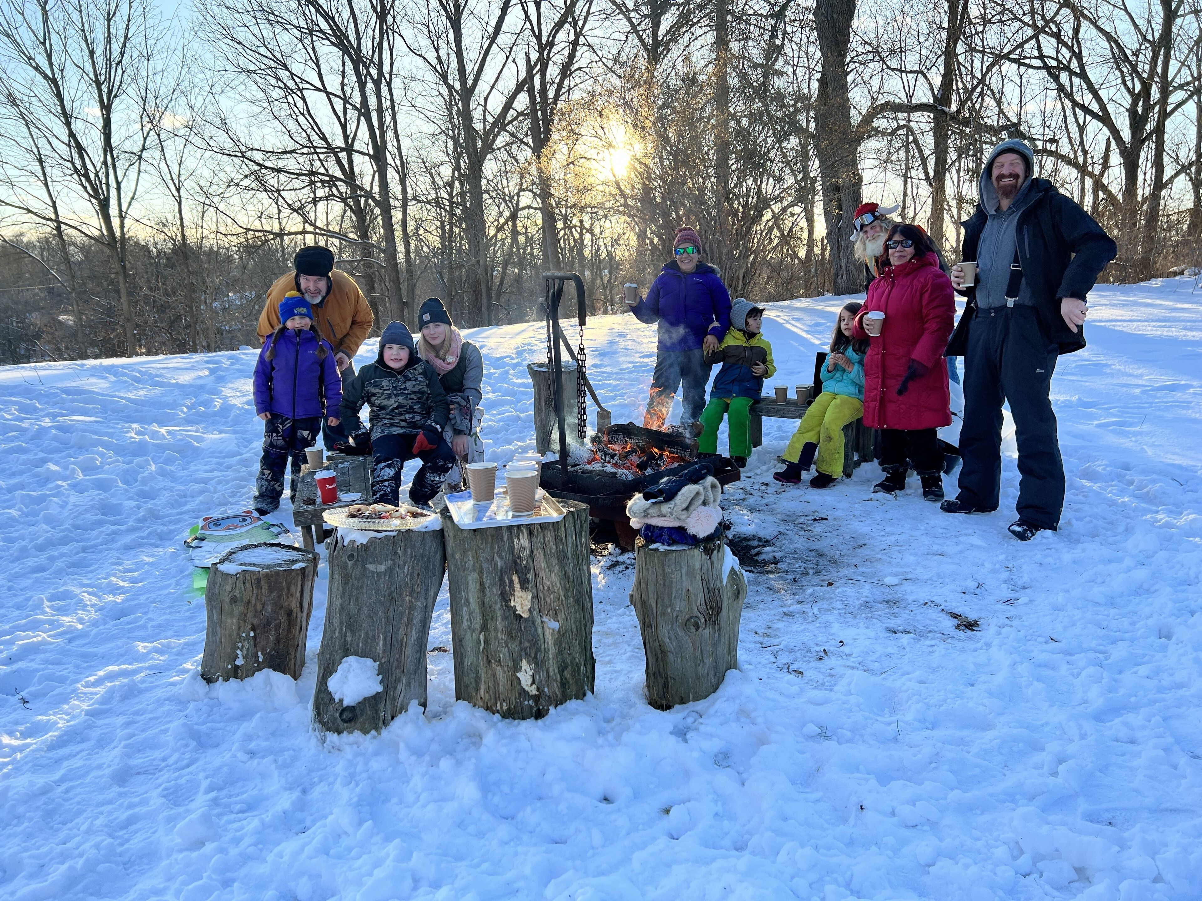 Um grupo de pessoas reunido em volta de uma fogueira em um ambiente externo com neve.