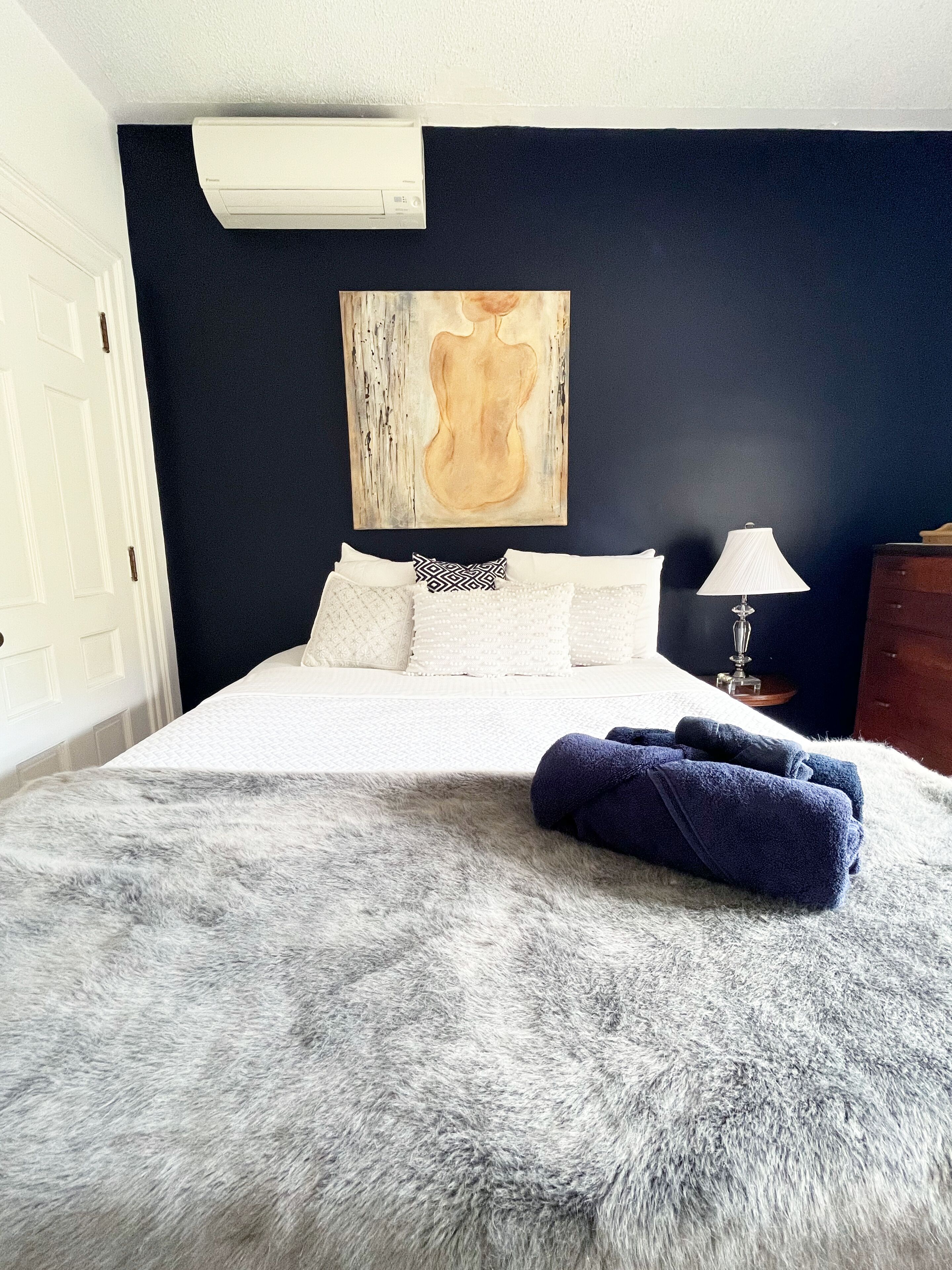 Een slaapkamer met een groot bed, een zachte grijze deken en een schilderij aan de muur.