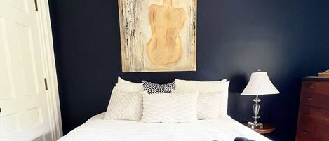 Een slaapkamer met een groot bed, een zachte grijze deken en een schilderij aan de muur.