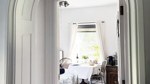 A hallway leading to a room with a bed, a table with a lamp, and a window with curtains. - Clonmel Castle (Norfolk County)