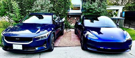 Two blue cars parked in a driveway with a brick wall and greenery in the background.