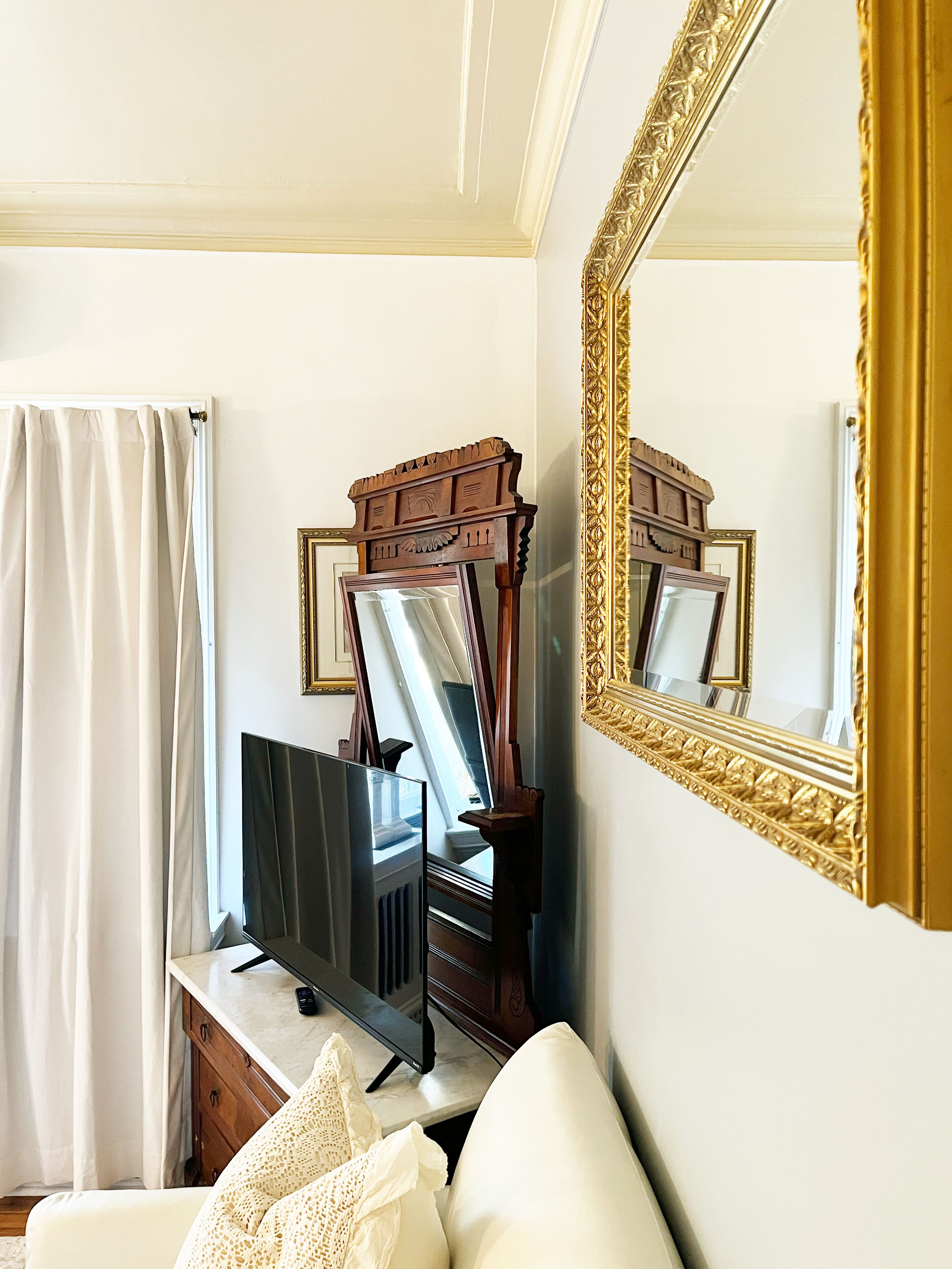 Une pièce avec un grand miroir, une commode en bois, un téléviseur et un canapé blanc.