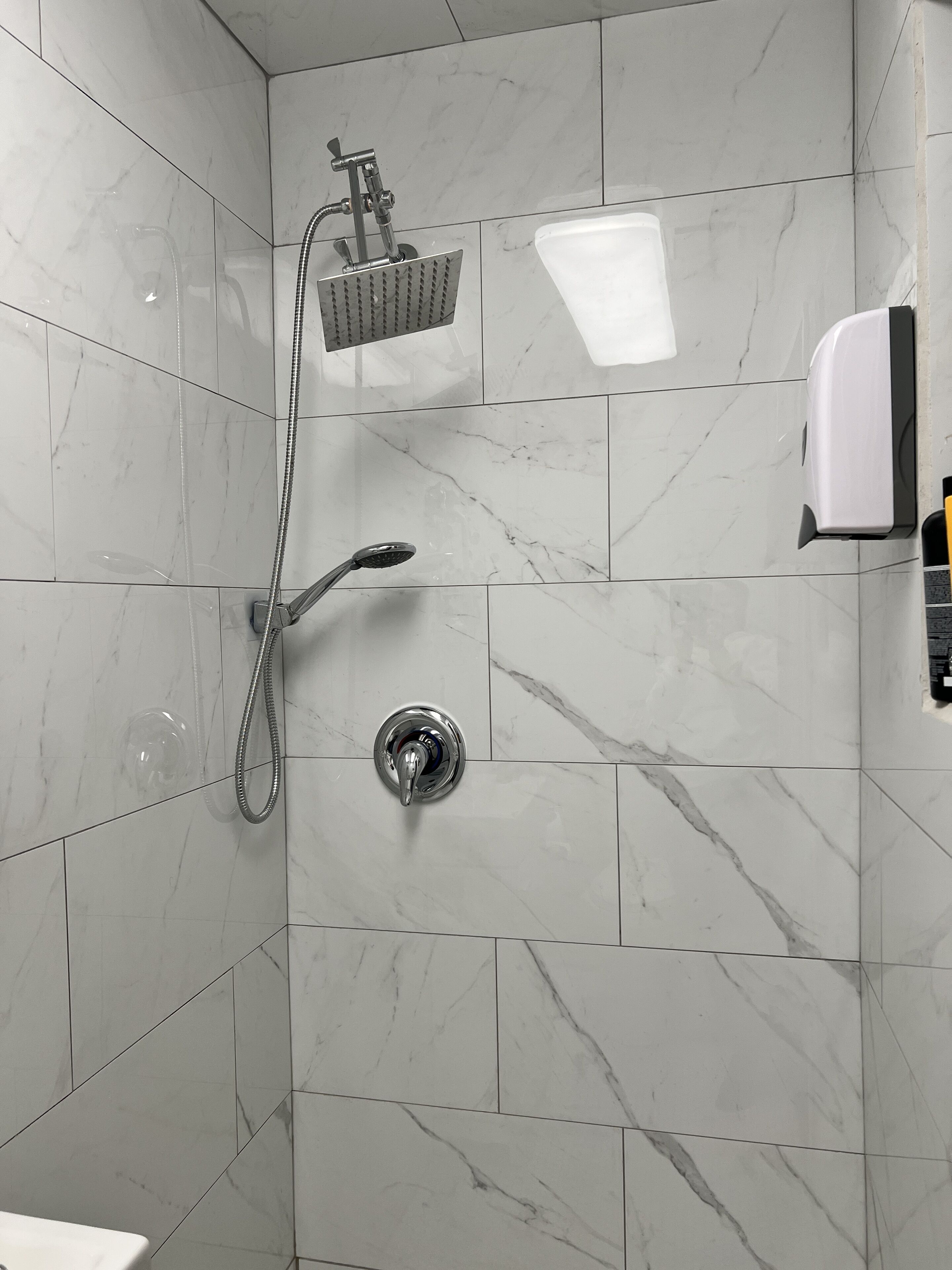 Une salle de bain moderne équipée d’une douche, d’un sèche-mains et d’un distributeur de savon.