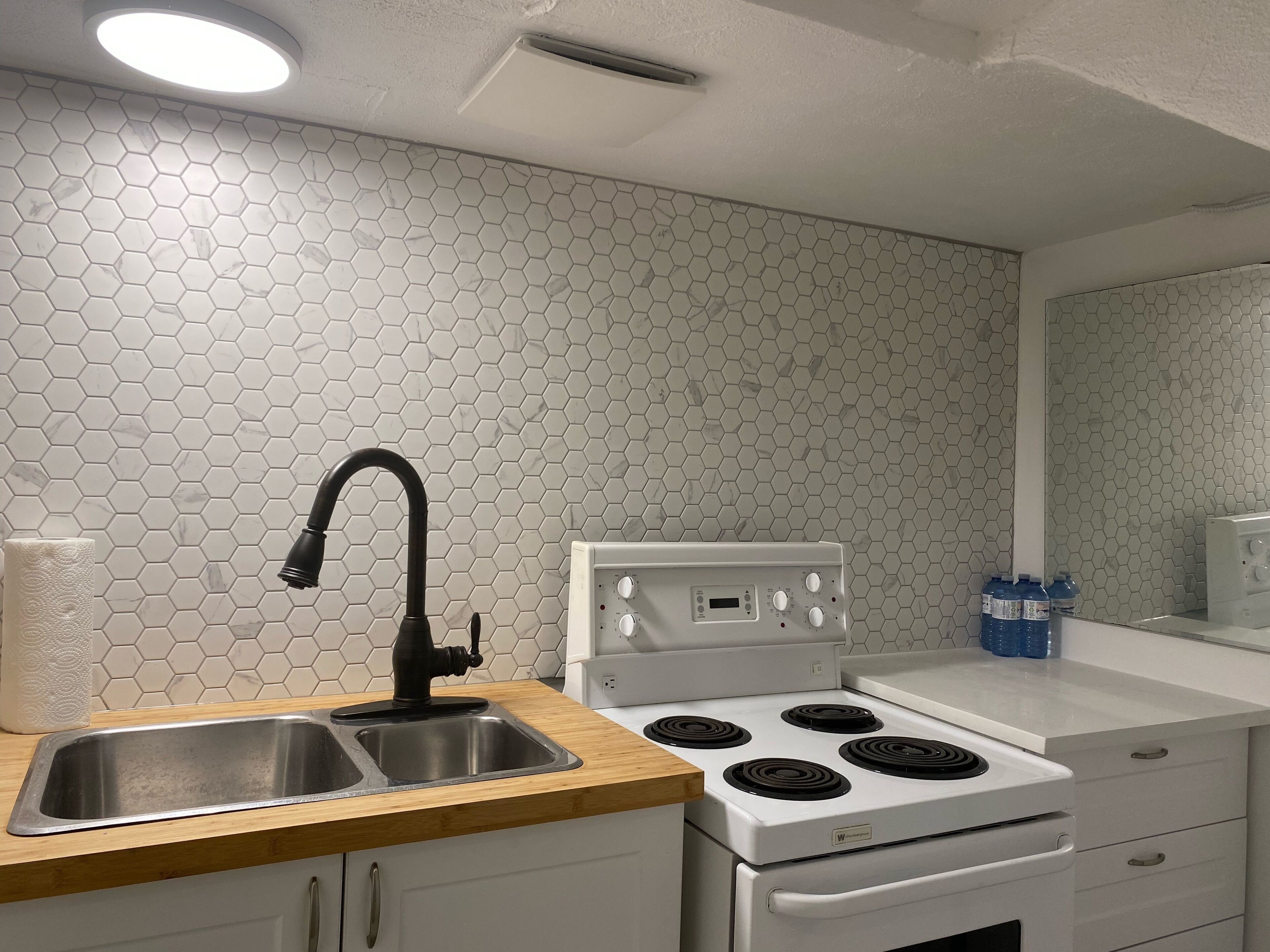 Una cocina con un lavamanos de acero inoxidable, un grifo negro, una estufa blanca con cuatro hornillas y una encimera blanca.
