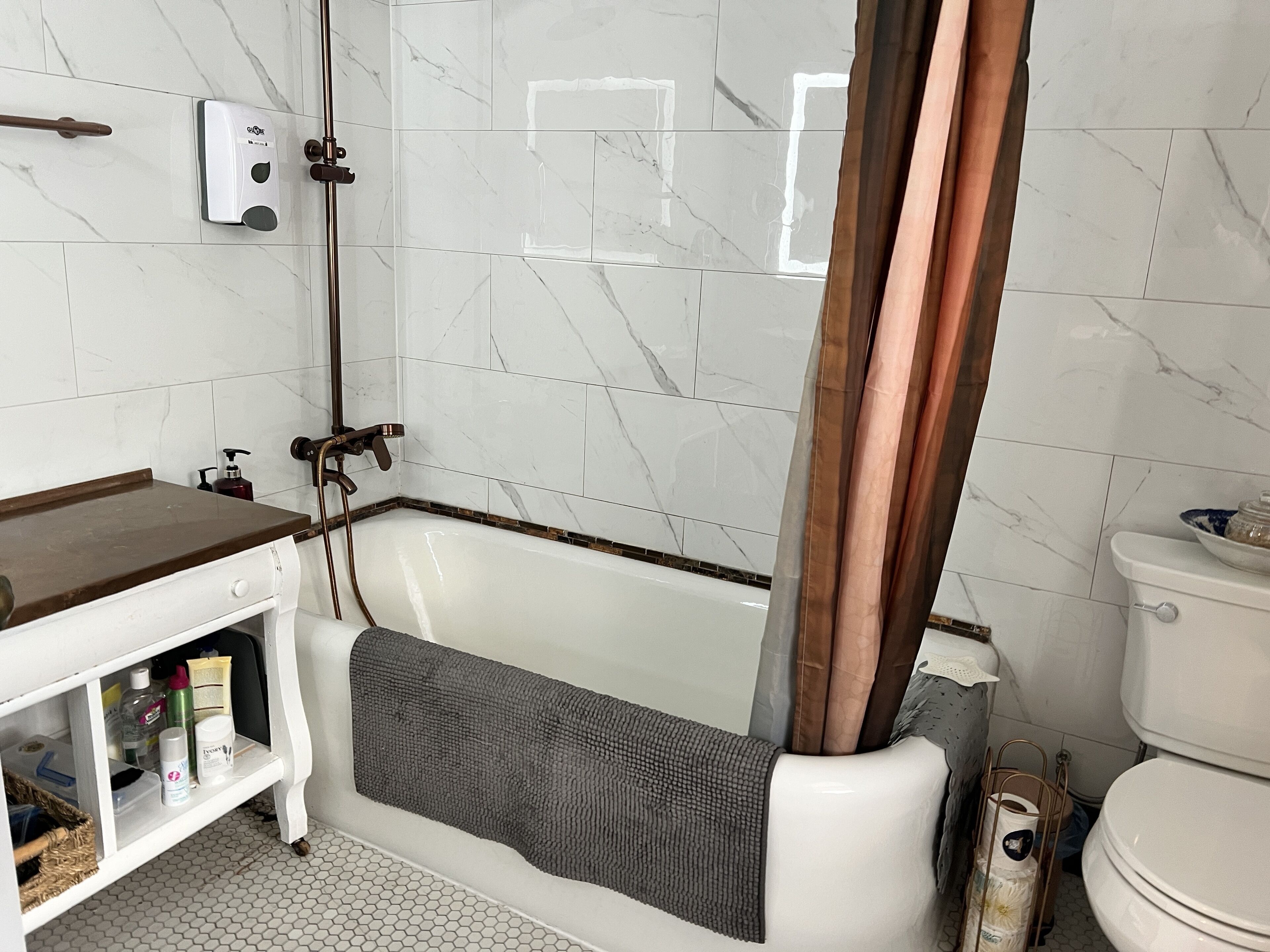Un baño con bañera, inodoro y dispensador de jabón en la pared.